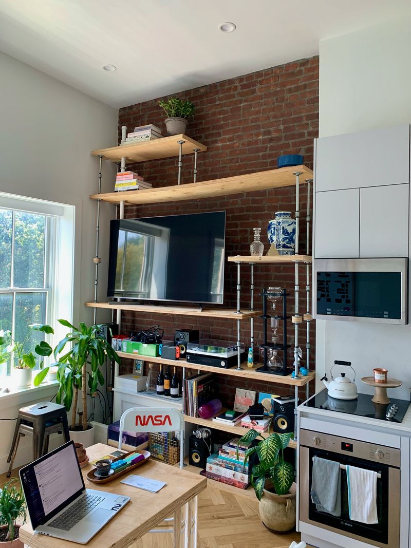 A wall-sized bookshelf made out of plywood and plumbing pipes against brick.