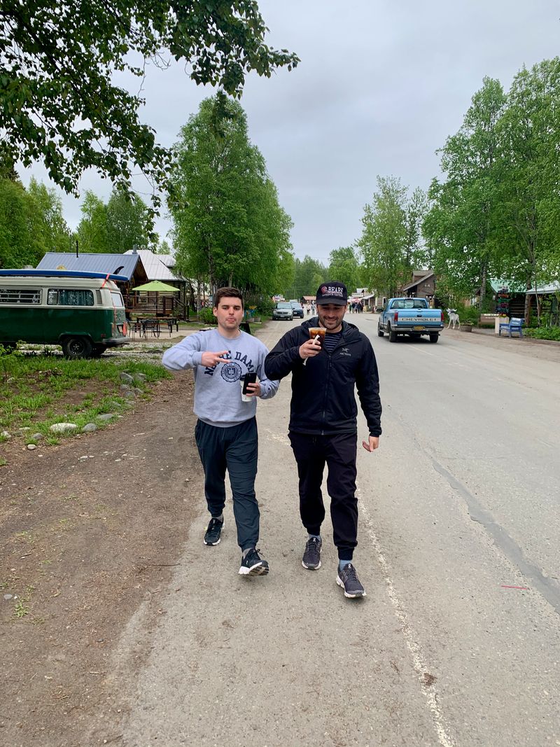 Two brothers walking through a small mountain town with fresh coffee; one peace sign, one cheers.